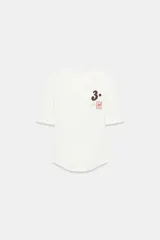 Camiseta de manga corta color blanco, con cuello redondo y bajo recto. Presenta un pequeño bordado y estampado en el pecho, incluyendo el número "3." y un pequeño cuadrado con un corazón.