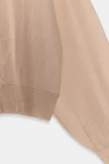 Chaqueta estilo bomber de punto color beige con acabado brillante, cuello redondo, manga larga con puños elásticos y cierre frontal con cremallera.