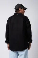 Camisa de manga larga estilo sobrecamisa, color negro, con corte oversize, cuello clásico, cierre frontal con botones y bolsillo frontal en el pecho.