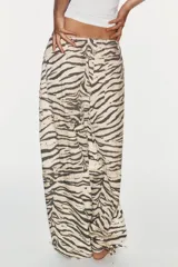 Pantalón de tiro medio con estampado animal print tipo tigre en tonos beige y negro. Presenta trabillas, cintura ajustable con cordones, bolsillos laterales y traseros, y bajo ajustable con cordón. Cierre frontal con cremallera y botón a presión.