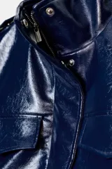 Chaleco azul marino brillante con efecto piel, cuello subido y manga sisa. Presenta trabillas en los hombros, bolsillos laterales y falsos bolsillos con solapa en el pecho. El bajo es abullonado con elástico y tiene forro interior a tono. El cierre frontal es con cremallera y botones a presión ocultos por una solapa.