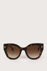 Gafas de sol con montura estilo cat-eye en estampado carey y lentes degradados en tono marrón. Presentan detalles metálicos dorados en las esquinas superiores de la montura.