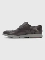 Zapato tipo Oxford estilo brogue con detalles perforados en la puntera y laterales. Presenta capellada de cuero en tono marrón oscuro, cordones al tono y suela de goma gris con diseño deportivo.