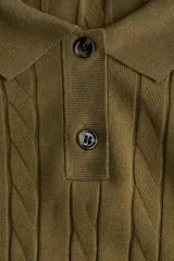 Sweater de punto color verde oliva, con cuello polo, tapeta de dos botones y manga larga. Presenta un tejido con diseño de trenzas verticales a lo largo del cuerpo y puños y bajo acanalados.