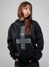 Buzo canguro negro con capucha, corte regular fit, de manga larga, con gran diseño de cruz frontal elaborado con tachas metálicas plateadas y tachas en el borde de la capucha.