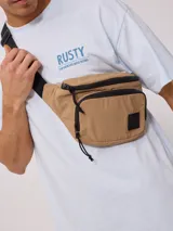 Riñonera de nylon color beige/camel, con acabado arrugado y detalles en negro, incluyendo cierres y tiradores de cordón. Posee un parche cuadrado negro con logo en el frente.