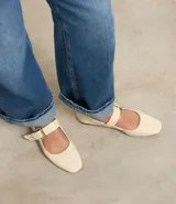 Zapatilla chatita de cuero color crema, con punta redonda, plantilla cómoda y tira con hebilla dorada en la parte superior.