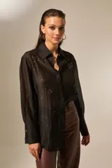 Camisa negra de lyocell, manga larga, con cuello camisero y botones frontales. La prenda está adornada con pequeños apliques de strass distribuidos por toda la tela.