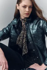 Camisa de cuero ovino verde metalizado, con cuello camisero y botones a presión con logo. Presenta un calce entallado.