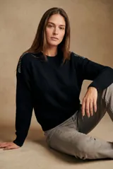 Sweater de lana color negro, de corte oversize, con cuello redondo, mangas largas y detalle de apliques metálicos en los hombros.