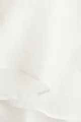 Blusa de ramio color blanco, con cuello redondo y cierre frontal de botones nacarados. Presenta un diseño de corte holgado con canesú fruncido en hombros y espalda, y mangas largas amplias que aportan volumen a la silueta.