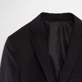 Chaqueta de traje de corte slim fit en color negro, con cierre frontal de dos botones, solapas clásicas y bolsillos laterales con solapa.