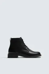 Bota de cuero negro con cordones tipo derby, parte superior lisa y plantilla interior de piel. Presenta horma cuadrada y suela con ligero tacón.
