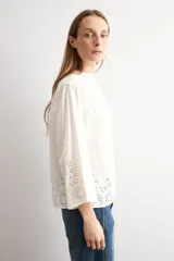 Blusa blanca de algodón con diseño de encaje bordado tipo broderie en el cuello, mangas y ruedo. Presenta mangas tres cuartos acampanadas y un corte holgado.