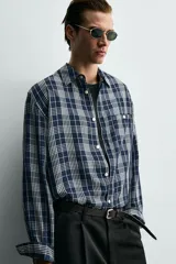 Camisa de corte relajado confeccionada en tejido fluido con mezcla de viscosa y acetato. Presenta un diseño a cuadros, cuello solapa, manga larga con puños abotonados, bolsillo plastrón en el pecho y cierre frontal con botones.