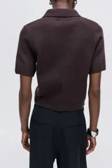Saco de punto suave con cuello camisero y cierre frontal de botones. Presenta mangas cortas y terminaciones acanaladas en puños y ruedo.