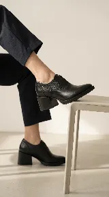 Zapato tipo slip-on color marrón, confeccionado en cuero natural con combinación de texturas lisas y grabadas. Presenta un diseño de punta almendrada, taco cuadrado de madera y suela dentada.