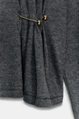 Top de cuello alto y manga larga, confeccionado en tejido de algodón gris melange. Presenta un diseño con frunces laterales ajustados mediante un aplique metálico decorativo.