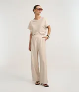 Pantalón de mujer de tiro alto, corte wide leg, color beige con finas rayas verticales en tono oscuro. Presenta cintura elástica fruncida y caída fluida.