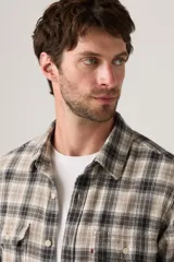 Camisa de manga larga a cuadros en tonos beige, marrón y negro, con dos bolsillos frontales con solapa y botones blancos.