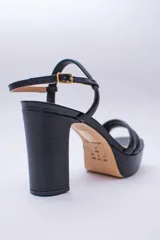 Sandalia de cuero con plataforma y taco cuadrado alto. Presenta una tira delgada en el tobillo con cierre de hebilla metálica y dos tiras acolchadas en la parte frontal.