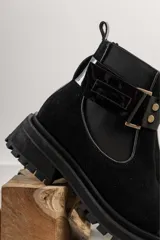 Bota tipo Chelsea de cuero marrón con suela track negra de goma. Presenta paneles elásticos laterales y una costura reforzada en la puntera. Incluye una correa de cuero desmontable con hebilla metálica.