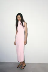 Vestido midi de cuello subido y sin mangas, confeccionado con un diseño drapeado lateral que aporta textura y movimiento a la prenda. Presenta un corte entallado y cierre de cremallera oculta en la espalda.