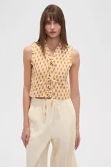 Musculosa de viscosa con textura de punto smock, estampado de flores pequeñas, cuello profundo con cierre de lazos frontales y detalles de volados en las sisas.