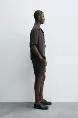 Bermuda de hombre, corte regular fit, color oscuro con patrón de rayas verticales finas en tono marrón claro. Presenta cintura elástica ajustable con cordón interior, bolsillos frontales y un bolsillo trasero de plastrón.