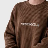 Sweater de punto acanalado en color marrón, con cuello redondo y logo bordado en el pecho. Presenta un diseño de corte holgado con mangas largas.