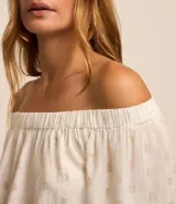 Blusa blanca con lunares dorados, escote hombro a hombro y mangas largas abullonadas con ajuste en los puños.