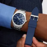 Reloj analógico Guess con caja de acero inoxidable plateado y esfera azul con acabado sunray, índices y números romanos. Incluye una correa de acero inoxidable plateado y una correa de silicona azul intercambiable.