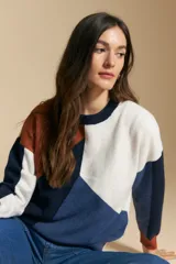 Sweater de tejido de punto con diseño geométrico de bloques de color en tonos tierra, marrón, ocre y blanco. Presenta cuello redondo, mangas largas y un corte relajado.