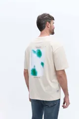 Remera de manga corta color gris oscuro con cuello redondo y calce regular. Presenta un estampado artístico rectangular en la espalda con diseño de manchas en tonos azules y texto descriptivo.