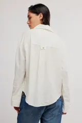 Blusa de lino color blanco crudo, de corte relajado, con cuello clásico, cierre frontal de botones, bolsillo en el pecho y mangas largas con presillas para arremangar.