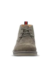 Botines tipo chukka Hush Puppies modelo New Safari, confeccionados en gamuza color gris. Presentan cierre de cordones, suela de goma con costura decorativa y detalle de tirador en el talón con franjas rojas y negras.
