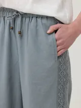Pantalón de corte amplio y tiro alto, confeccionado en una mezcla de lino orgánico y viscosa. Presenta cintura elástica con cordón ajustable y detalles de encaje broderie tono sobre tono en los laterales y en el ruedo.