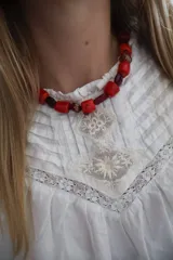 Gargantilla corta elaborada con cuentas de semillas en tonos rojos y borgoña, intercaladas con pequeñas piezas metálicas con detalles grabados.
