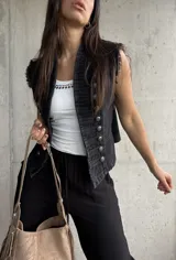 Chaleco negro de denim estilo militar, con doble botonadura metálica frontal, cuello alto y detalles deshilachados en las sisas.