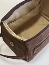Neceser de cuero gamuzado color marrón, con diseño de doble cierre y manija lateral. Presenta detalles en cuero liso y logo de la marca grabado en el frente.