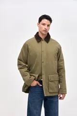 Campera de gabardina color verde oliva con cuello de pana en tono marrón oscuro. Presenta cierre frontal oculto por cartera con botones a presión, bolsillos laterales con solapa y bolsillos en el pecho. Interior acolchado con diseño capitoneado.