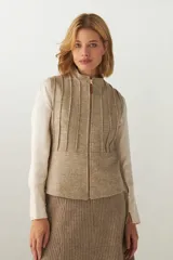 Chaleco corto entallado de lana fina sin teñir, color marrón claro jaspeado, con cierre frontal y alforzas verticales en delantera y espalda.