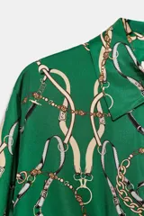 Camisa de cuello solapa y manga larga con puños, confeccionada en tejido satinado con estampado de cadenas. Presenta cierre frontal con botones y bajo ajustable mediante cordones.