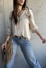 Camisa beige de manga larga con cuello en V, cierre frontal de botones y delicados bordados florales en marrón en la zona del pecho y en los puños.