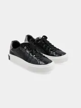 Sneaker de mujer con diseño de textura tipo cocodrilo en color negro, con suela de plataforma blanca y detalle de logo en el talón de la suela. Incluye un detalle en color plateado en la parte superior del talón.