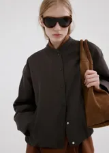 Chaqueta bomber oversize color verde oscuro con cuello mao, manga larga y cierre frontal de botones a presión.