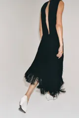 Vestido midi de Zara Woman Collection color negro, sin mangas, con cuello redondo y espalda abierta. Presenta un diseño asimétrico en el bajo adornado con flecos a tono, y cierre trasero con cremallera y botón.