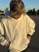 Hoodie de color blanco off-white con diseño de capucha, bolsillo frontal tipo canguro y bordado en relieve con el texto ITTAI STARS y un logo caligráfico.