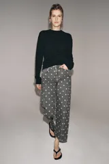 Jeans de tiro medio con corte relajado y largo al tobillo. Presenta un diseño de cinco bolsillos, cierre frontal con cremallera y botón metálico, y un estampado integral de lunares blancos sobre fondo gris oscuro.