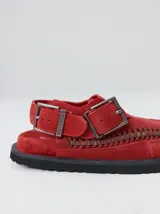 Slipper tipo guillermina confeccionada en gamuza color marrón, con plataforma de goma negra y doble hebilla ajustable. Presenta un pespunte decorativo en el borde inferior y cuenta con interior recubierto en cuero.